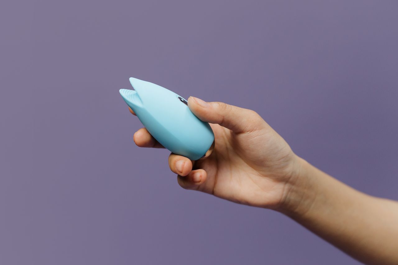 A blue silicone sex toy held in hand against a solid purple background, promoting self-love and sexuality.